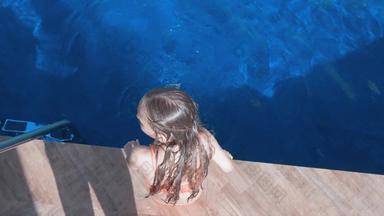 女孩坐着池一边摇摆腿游泳池水户外开销视图前视图女孩溅腿蓝色的水游泳池度假胜地酒店