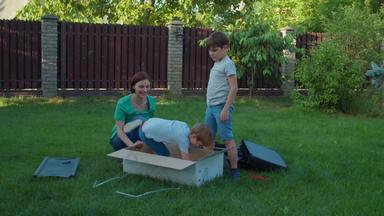 妈妈。孩子们有趣的大盒子后院阳光明媚的一天快乐家庭戏剧交付纸板盒子草慢运动替身拍摄