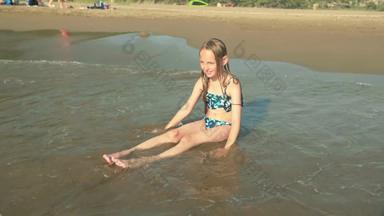 可爱的女孩泳装坐着桑迪海滩享受海波