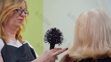 发型师梳理头发刷弄头发高级女人美工作室理发师梳理金发碧眼的头发刷完成发型成熟的女人发型概念