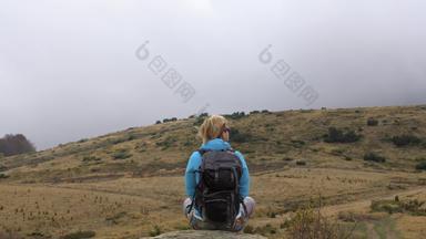 女徒步旅行者蓝色的夹克背包坐着岩石享受视图多风的多云的一天旅行健康的生活方式在户外秋天季节