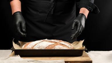 老板<strong>黑色</strong>的乳胶<strong>手套</strong>持有烘焙表烤面包黑麦面包<strong>黑色</strong>的背景