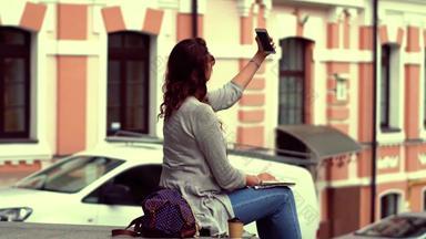 年轻的漂亮的旅游女人坐着栏杆使自拍照片