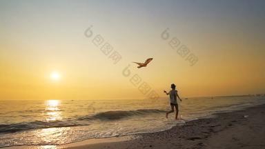 可爱的快乐男孩他运行海海岸海滩玩飞行风筝充满活力的橙色日落电影替身拍摄慢运动