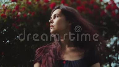 一位美丽的黑发年轻女子站在盛开的红玫瑰丛边，眺望远方
