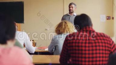 高中老师帅哥正在和坐在教室里的桌子旁微笑的学生交谈。 教育