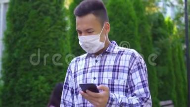 戴着医用口罩的亚洲年轻人在公园里咳嗽，用智能手机慢吞吞地说