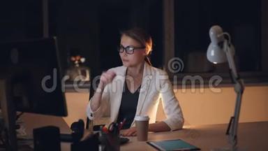 戴着眼镜和西装的疲惫的金发女郎深夜在电脑上工作，喝着外卖咖啡，感到疲倦和疲惫