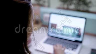 年轻的黑发女人正在浏览网站，用笔记本上网购物，在家里的透明房间里喝咖啡