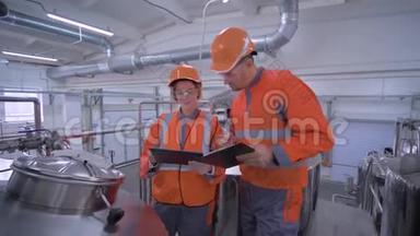 在讨论质量问题时，工厂工人中的女工人带着戴头盔的男工人带着平板电脑检查工厂
