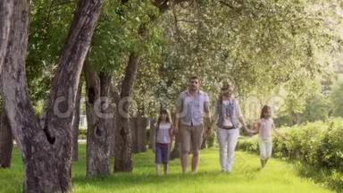 快乐的一家人走在夏天的公园里，靠近盛开的苹果树。 父亲、母亲和两个女儿