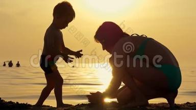 快乐的母亲和孩子在海滩上玩沙子对抗日落。