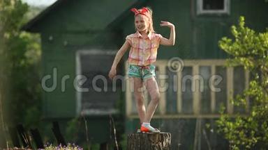 一个可爱的小女孩在乡间房子的院子里的树桩上跳舞。 很开心。