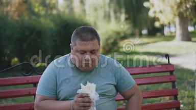 一个胖子在长凳上吃东西，看着他有害可口的快餐