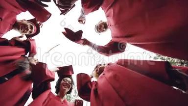 低角度拍摄的女生和男生毕业的学生扔灰泥板在天空和笑。 庆祝活动