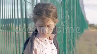 无家可归的难民儿童。 高加索小女孩站在金属栅栏前的肖像，她既不快乐又怨恨。