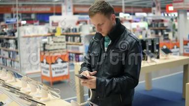 穿黑色皮夹克的年轻人正在商店里挑选一部<strong>新手机</strong>，检查它的工作原理