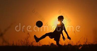 一个男孩在海滩上踢足球或踢足球的剪影，背景是美丽的日落