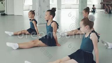 孩子们上<strong>舞蹈课</strong>。 小女孩坐在地板上，重复老师后面的动作