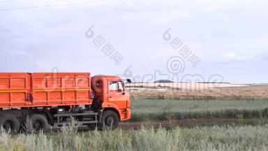 橙色，新的咆哮与拖车移动在乡村道路上的绿色和黄色的田野背景。 场景。 带拖车的卡车