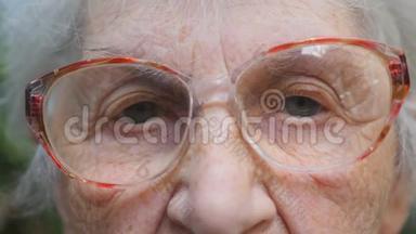 戴眼镜的老妇人看着摄像机。 一位有皱纹的老太太的眼睛。 特写肖像画