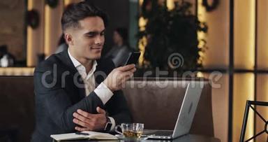 在咖啡馆工作的年轻商人。 使用智能手机和笔记本电脑的自由职业者。 成功的职业生涯，IT，自由职业者的概念。