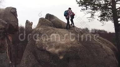 运动的男孩和女孩带着旅游背包爬上岩石山，然后登上山顶，牵着手