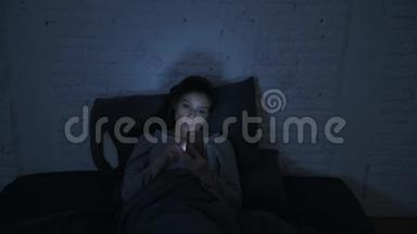 一张30多岁的西班牙裔年轻女子的正面照片，她躺在床上，深夜用手机看着