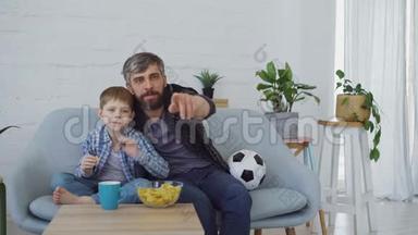 足球迷们留着胡子的男人和他的小孩在家里看电视，庆祝进球和吃<strong>薯片</strong>