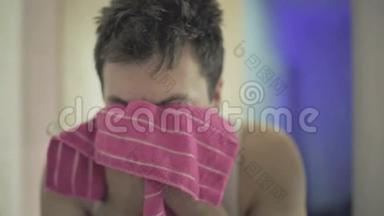年轻人洗脸，在镜子前用毛巾擦脸。