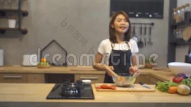 年轻的亚洲女人在厨房里用相机录制视频。 微笑的亚洲妇女从事食品博客概念。