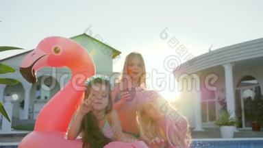孩子们在暑假穿着泳衣的名人，小女孩躺在游泳池附近的充气粉红火烈鸟上，被宠坏的富人