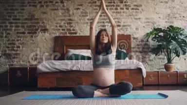 运动孕妇正在家中练习瑜伽，坐在卧室<strong>地板</strong>上的垫子上举手，把手掌<strong>放在</strong>一起