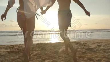 年轻夫妇正在海滩上跑步，男人在日落时拥抱和旋转他的女人。 女孩跳到男友怀里