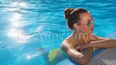 一位身穿泳衣的年轻女子正在游泳池里喝着清凉的水，一个炎热的夏日