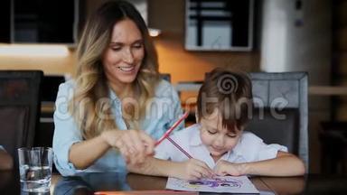 美丽的妈妈帮助她的儿子用彩色铅笔画图像。 帮助培养孩子`想象力。