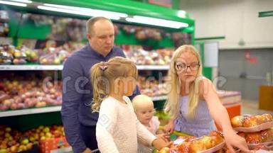 快乐的一家人在购物。 一家四口路过的水果店。 家庭在超市购物