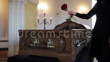 葬礼上悲伤的女人把红玫瑰放进棺材里