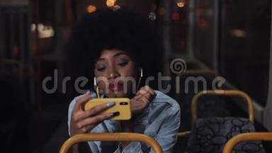 年轻的非洲裔美国妇女在公共交通工具上看智能手机视频。 晚上。 特写镜头。 城市