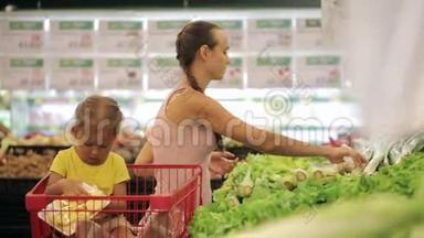 年轻的母亲带着小女儿在手推车里挑选<strong>超市</strong>里的<strong>蔬菜</strong>