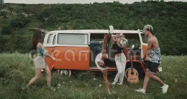 充满魅力的年轻一群朋友在大自然中跳舞，在田野的中央，在一辆复古的<strong>面包车</strong>后面。 4k
