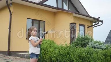 可爱的小女孩拿着一根水管，在给草坪浇水时摇动它