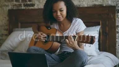 迷人的非洲裔美国少女，专注于学习使用笔记本电脑弹吉他，坐在床上