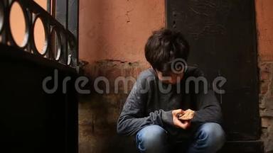 一个无家可归的少年在炉栅的背景下，在门口吃面包皮