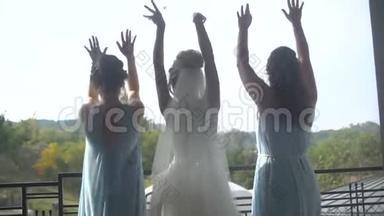 优雅的新娘穿着奢华的长裙，两位伴娘穿着蓝色的裙子，她的后景正在幸福地跳舞