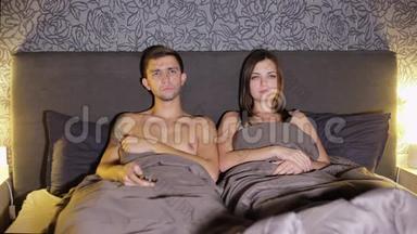年轻夫妇，男人和女人，睡前在卧室的床上看电视。