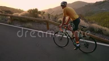 一个戴着头盔和运动装备的专业骑自行车的人在日落时缓慢地骑在山区公路上。 Stadicam