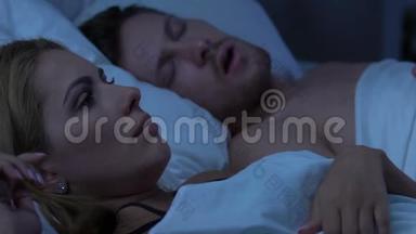 一对睡在床上的夫妇，不高兴的妻子被丈夫的响亮的呼噜声吵醒了