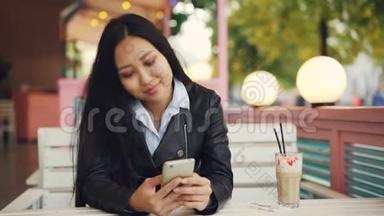 现代的亚洲女人正在使用智能手机，在风和日丽的秋日在街头咖啡馆里给朋友发短信