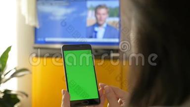 一个女人正在看电视，拿着一台绿色屏幕的智能手机。 在电视节目上的新闻。
